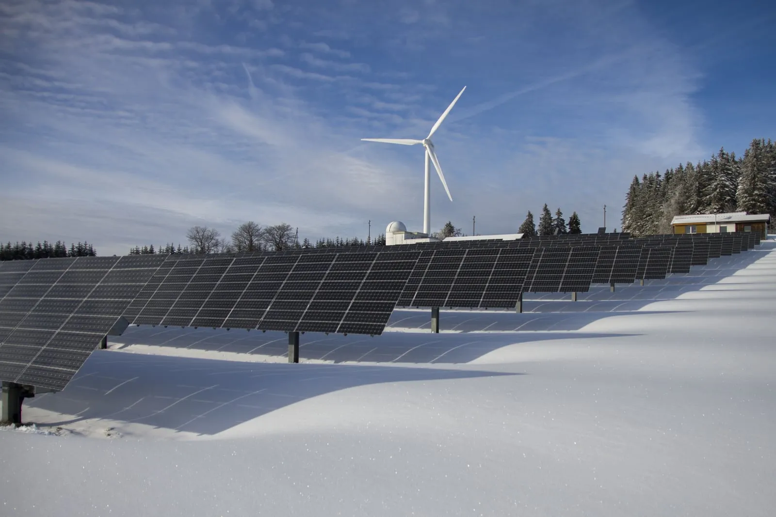 Planta fotovoltaica cubierta de nieve con un aerogenerador al fondo