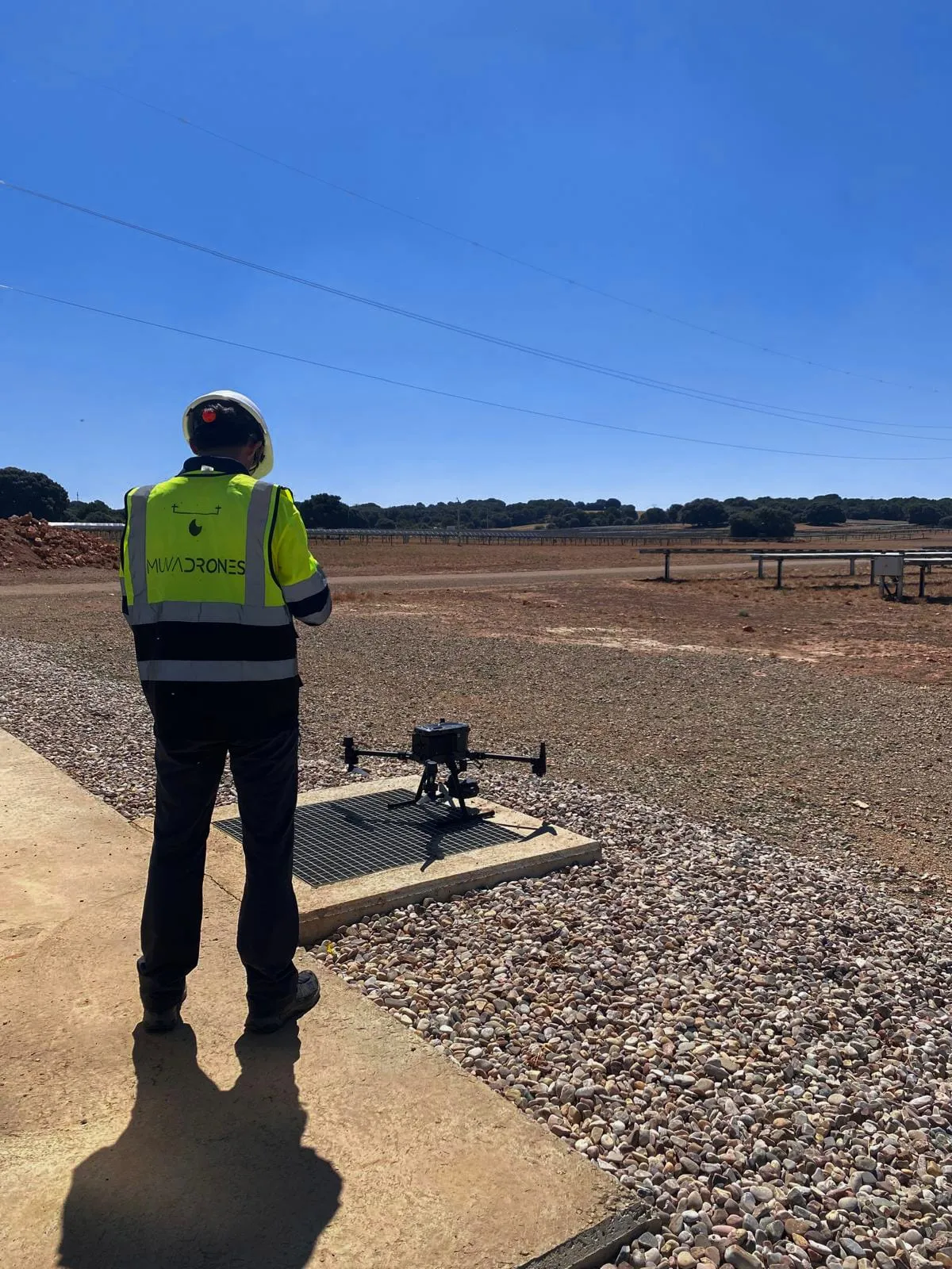 Piloto de MUVADRONES junto al dron posado, con la planta fotovoltaica al fondo